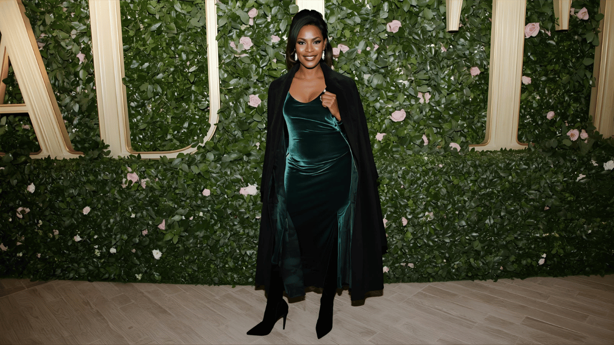 A stylish woman at a winter event wearing an emerald green velvet midi dress with black heeled boots, long coat draped over her shoulders, elegant evening ambiance.